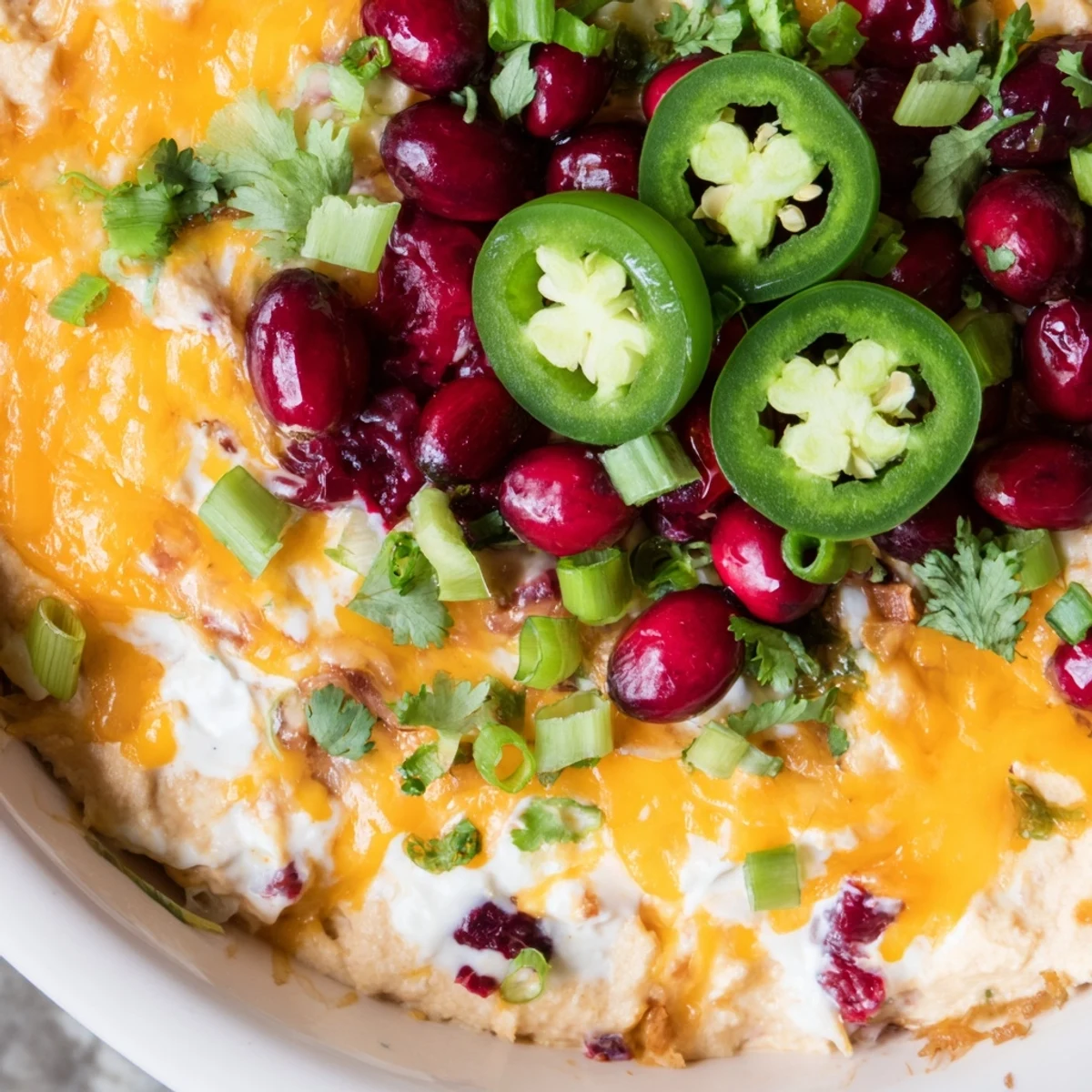 Creamy Cranberry Jalapeño Queso Dip bubbling with cheeses and colorful garnishes.  