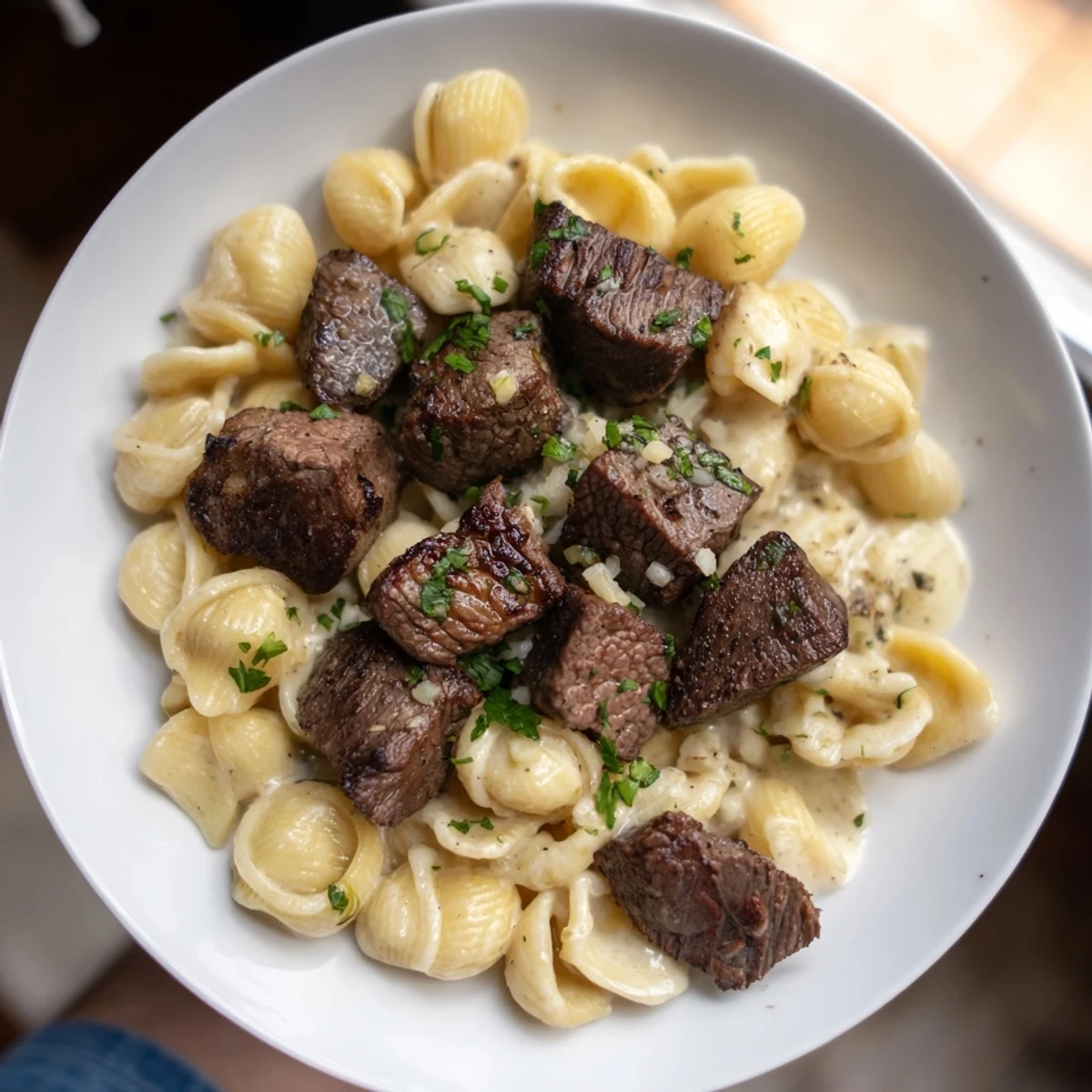 Garlic butter steak bites glistening on a plate, alongside creamy, cheesy pasta shells.