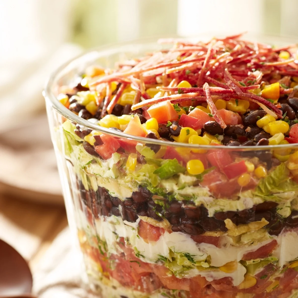 A clear glass bowl showcases the Southwest Sunset Palette, a layered salad with fresh garnishes.