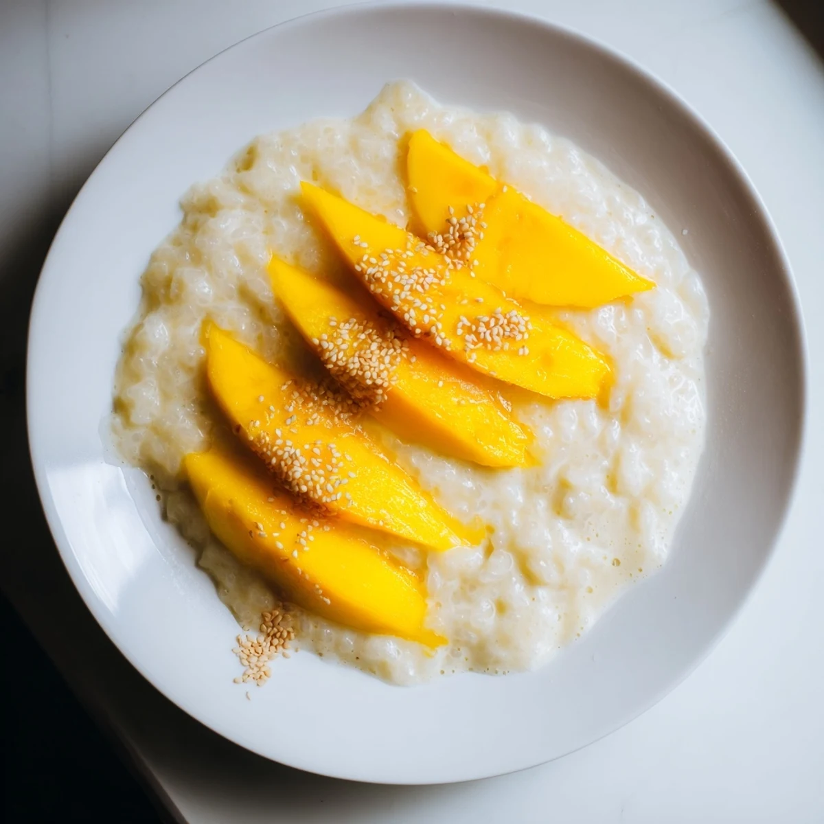 Golden mango slices next to creamy, coconut-infused Thai Mango Sticky Rice ready to be enjoyed.