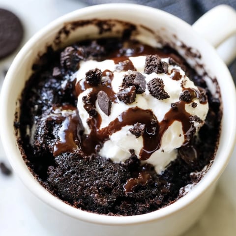 A warm, fudgy Oreo mug cake, ready to eat, topped with whipped cream and crushed Oreos.