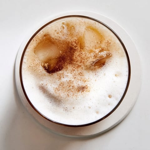 A glass of iced chai tea with cold foam, garnished with a sprinkle of cinnamon for a warm aroma.  