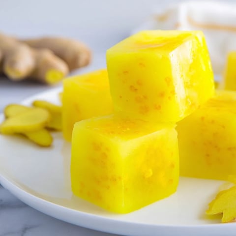 Bright yellow Lemon Ginger Turmeric Wellness Cubes glisten with condensation on a wooden board, ready to be popped into a glass of water for a refreshing immune boost.