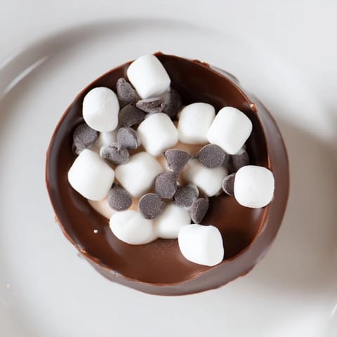 Fluffy marshmallows spilling from budget-friendly hot cocoa bomb cups, ready for a warm winter drink.