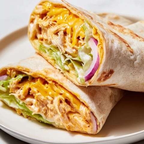 A close-up of a fresh Buffalo Ranch Chicken Wrap on a rustic wooden board, topped with a drizzle of creamy ranch and tangy buffalo sauce.  