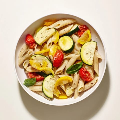 A fresh basil garnish crowns steaming Garden Veggie Pasta, plated beside a glass of Sauvignon Blanc for an easy summer dinner.